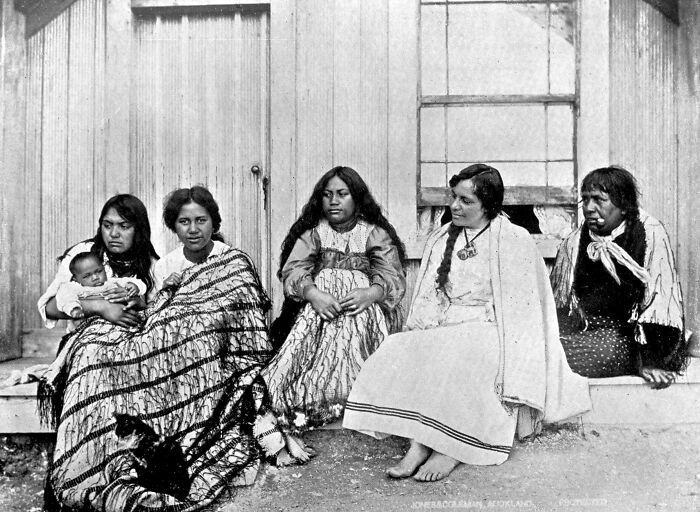 Five Māori women and a baby sitting outside a building, showcasing powerful portraits of Māori life a century ago.