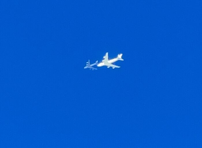 Two airplanes flying closely together in a clear blue sky captured as a rare coincidence photo.