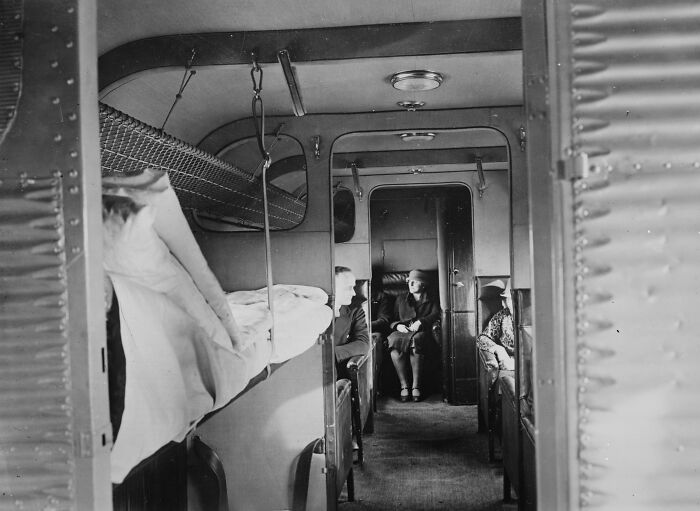 Vintage black and white photo of glamorous early airplane passengers seated in a luxurious cabin interior.