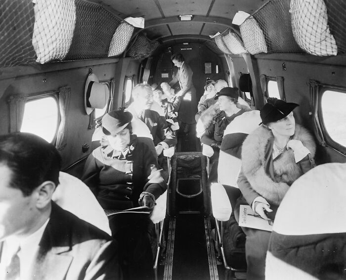 Vintage black and white photo of elegantly dressed passengers inside a glamorous airplane cabin from the early flying era
