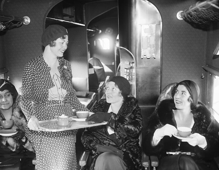 Three glamorous women enjoying tea served by a stylish flight attendant, capturing flying as an affair of pure glamour.