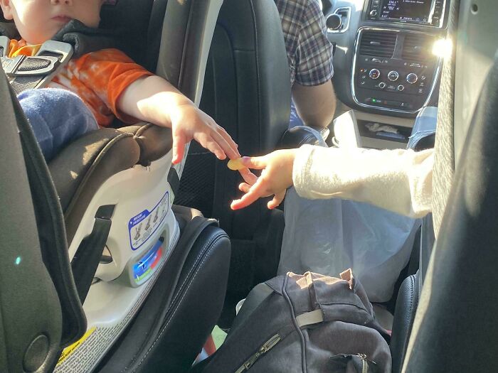 Two children in a car reaching out to touch fingers, creating an accidental Renaissance moment captured beautifully.