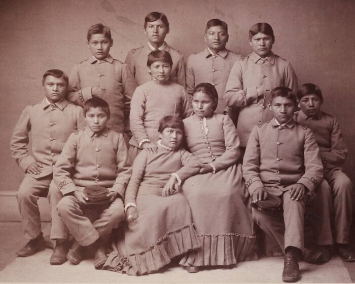 Group portrait of Native American children in early 1900s boarding school uniforms from haunting photos collection.