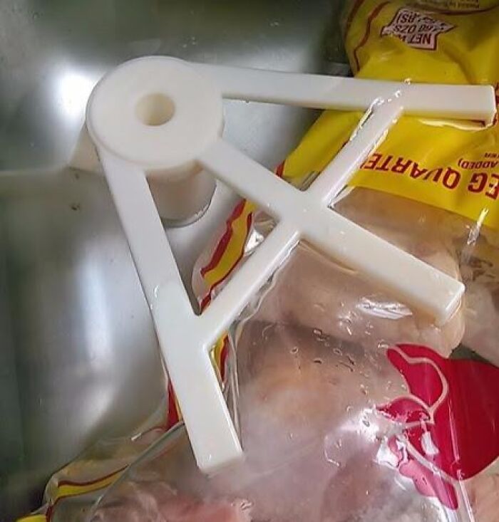 White plastic gadget placed in a sink holding a bag of frozen chicken, one of the genius gadgets tackling daily problems.