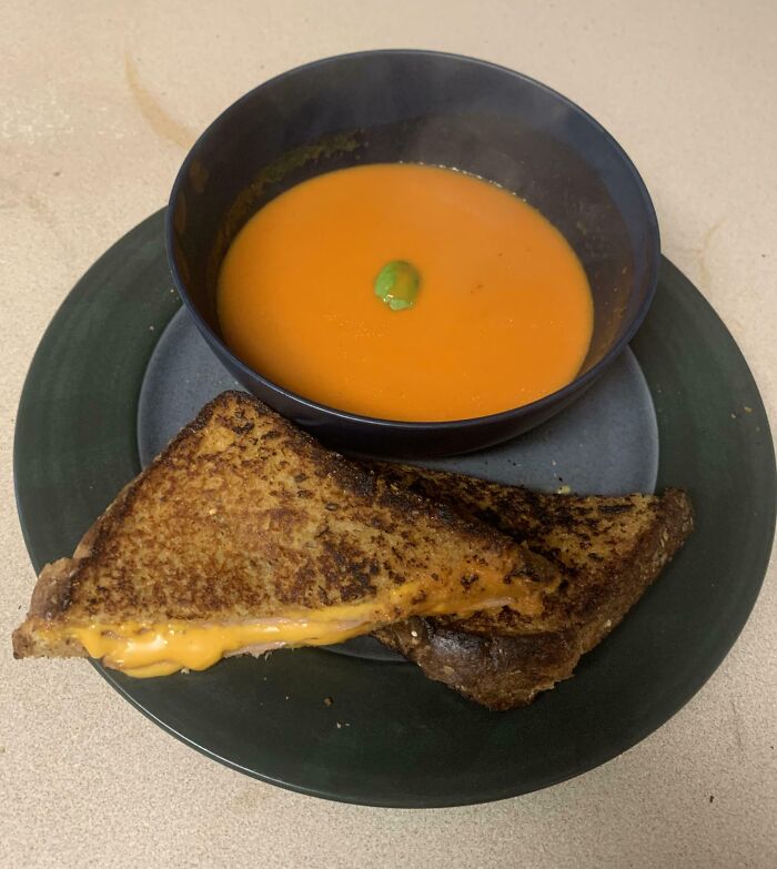 Grilled cheese sandwich with melted cheese and a bowl of smooth orange soup on a green plate in a harvesting setting.