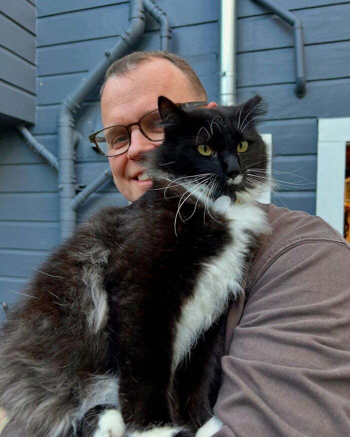 Man holding a tuxedo cat outdoors near a porch, highlighting the bond that led to building a house for the tuxedo cat. Man holding a tuxedo cat outdoors near a porch, highlighting the bond that led to building a house for the tuxedo cat.