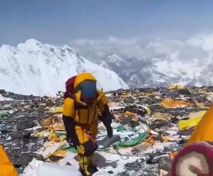 Montañista con ropa amarilla rodeado de basura en la nieve, mostrando fotos impactantes del aumento del consumismo.