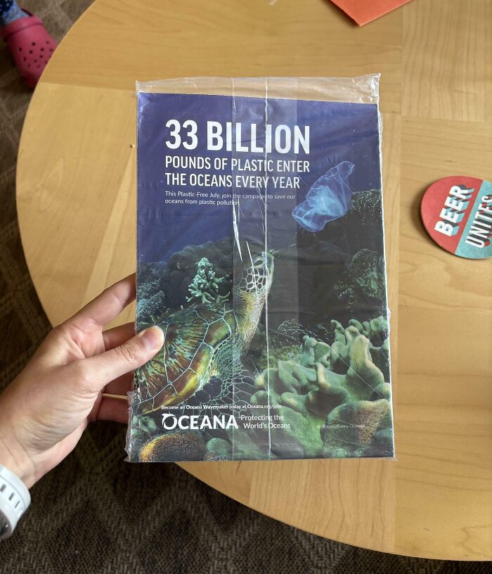 Mano sosteniendo folleto sobre daño a océanos por plástico, mostrando impacto del consumerismo y contaminación ambiental.
