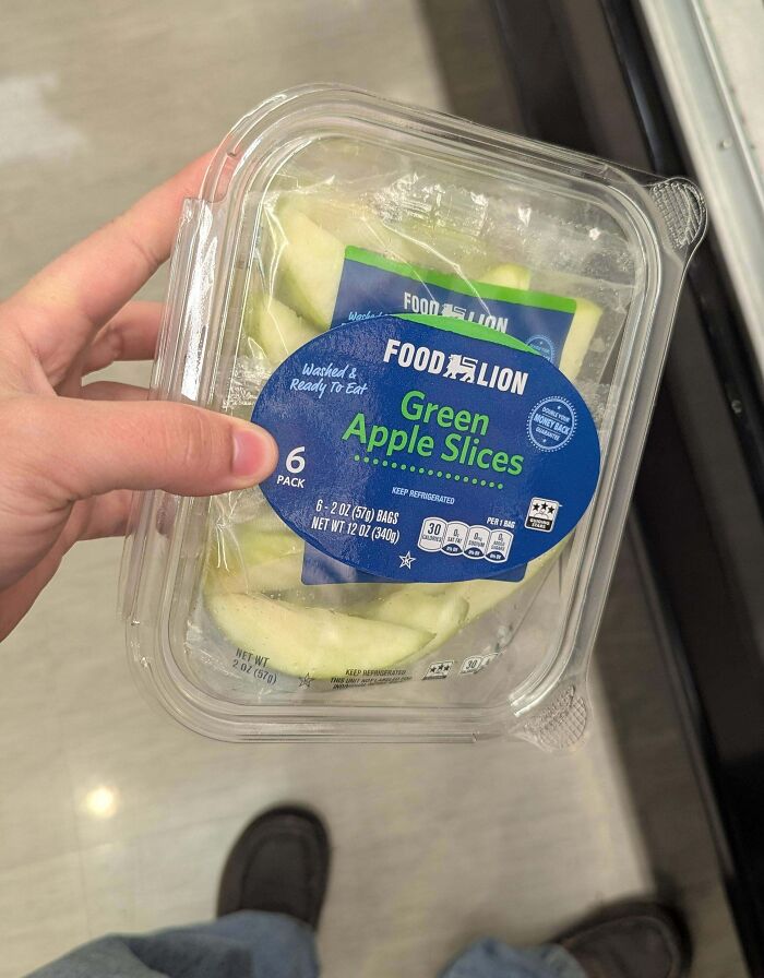 Hand holding a plastic container of pre-packaged green apple slices highlighting consumerism and excess packaging.