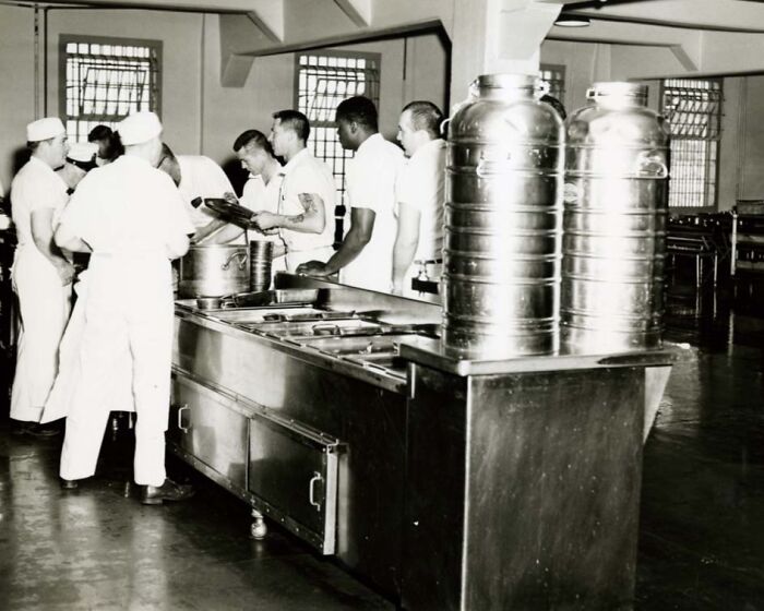 Prisoners in a cafeteria line receiving food trays inside Alcatraz, showing a rare glimpse into harsh life conditions.