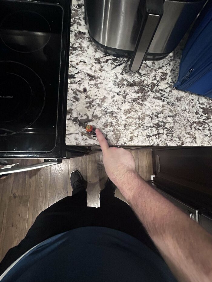 Person pointing at an unusually tiny tomato on a kitchen counter, showcasing a garden joke by Mother Nature.