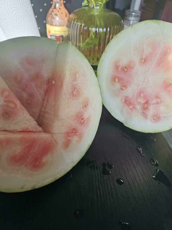 Half sliced unusual pale watermelon with light pink flesh and seeds on a dark surface, a garden surprise from Mother Nature.