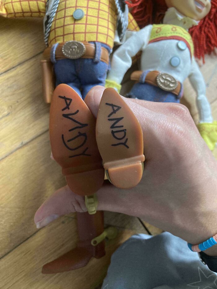 Two Toy Story Woody dolls held by hand showing the name Andy written on the soles of their shoes, moderately interesting detail.