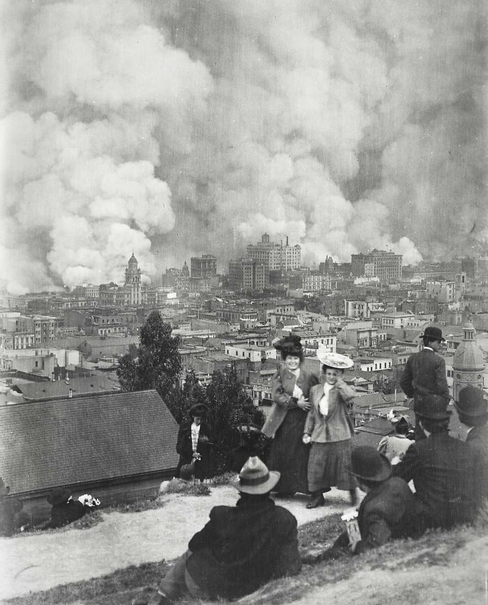 Crowd watching thick smoke rising over city during a historic 20th century tragedy, capturing triumph and tragedy moments.