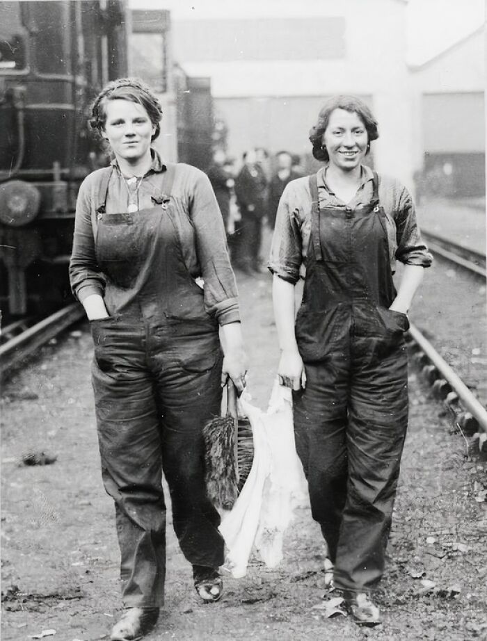 Two women factory workers in work overalls walking along railway tracks during WWI, showing how women changed everything.