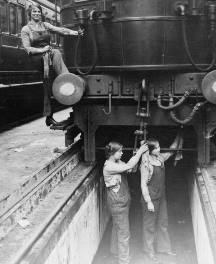 Women changing everything during WWI, working on and repairing a large train engine in a railway workshop.