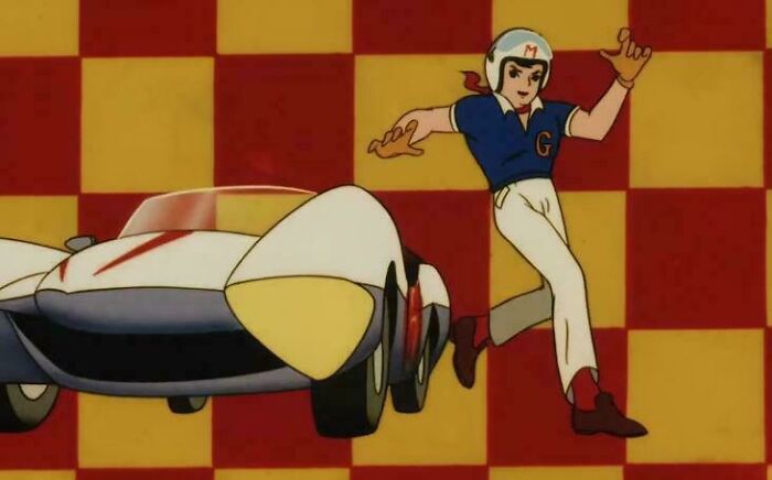 Animated character in vintage racing outfit next to classic race car, evoking nostalgia and old age memories.