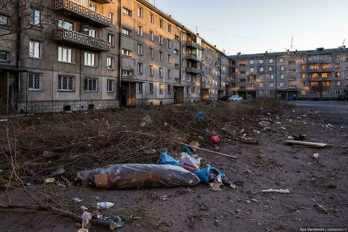 Run-down urban neighborhood with litter and debris scattered around neglected apartment buildings, illustrating urban hell conditions.