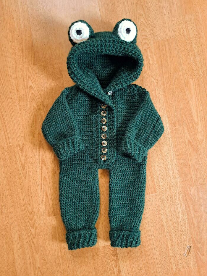 Crochet baby outfit with frog hood and buttons, showcasing intricate handmade craftsmanship by crochet enthusiasts.