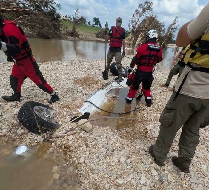 Rescue team inspects debris of a vehicle submerged by floodwaters, showcasing wild Mother Nature’s powerful impact.