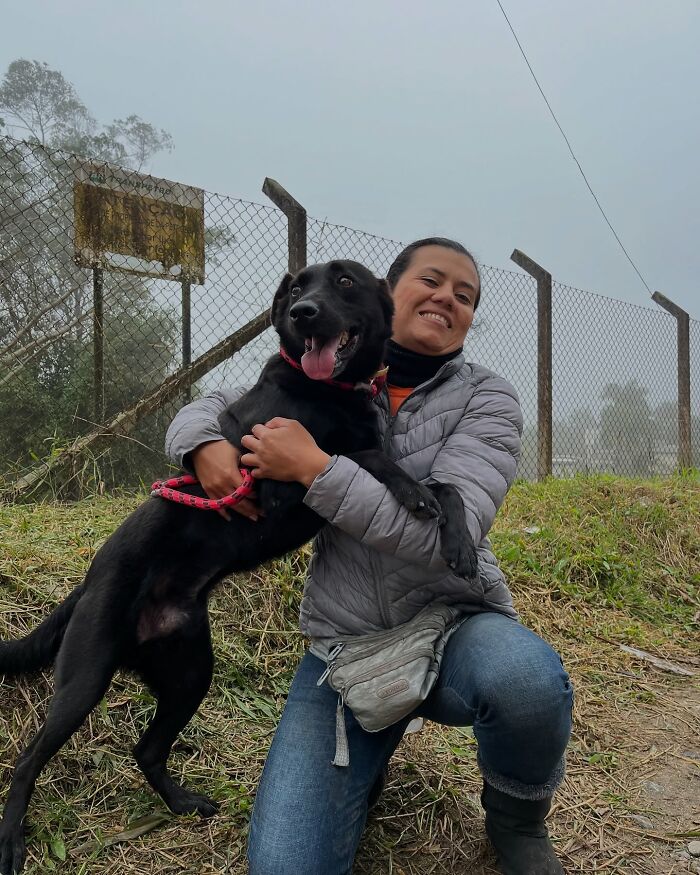 Woman hugging a happy black shelter dog outside near a fence, capturing the pure joy of shelter dogs on their weekly walks.