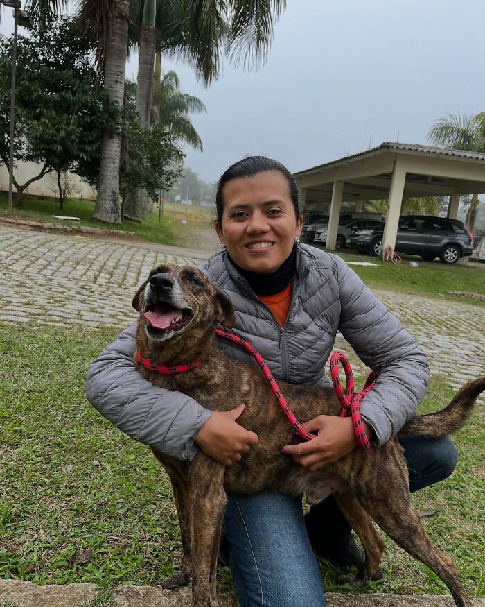Woman smiling and hugging a happy shelter dog on a grassy area during one of their weekly walks outdoors.
