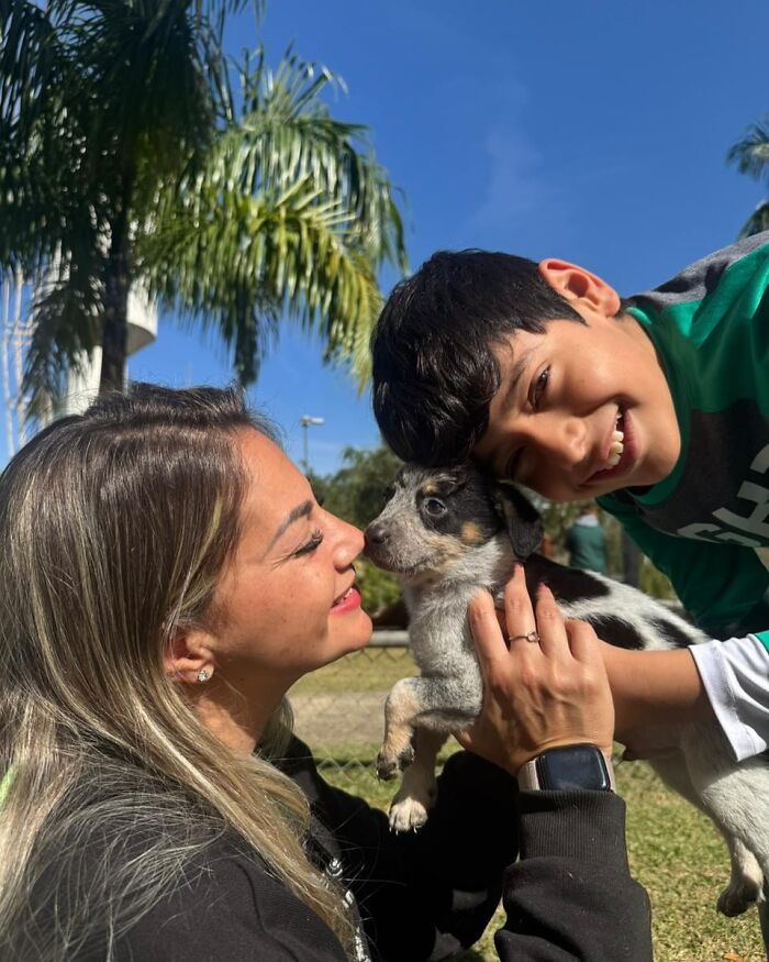 Woman and boy smiling at a happy shelter dog during joyful weekly walks outside on a sunny day with palm trees.