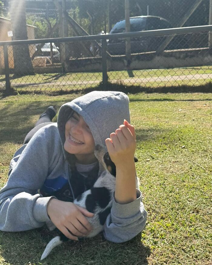 Teen smiling and cuddling a small shelter dog on the grass during a joyful weekly walk outdoors.