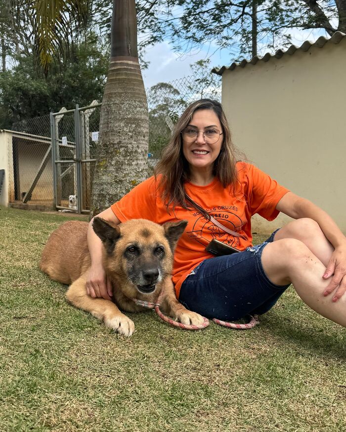Woman in an orange shirt sitting on grass with a shelter dog, capturing the joy of shelter dogs on their weekly walks.