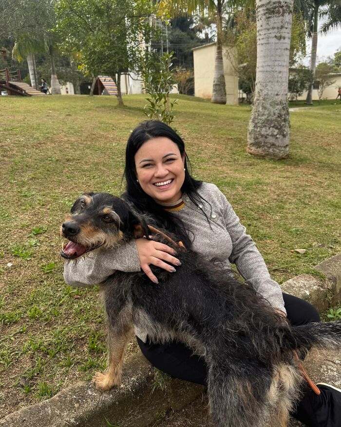 Happy woman hugging a joyful shelter dog outdoors during one of their weekly walks in a green park setting.