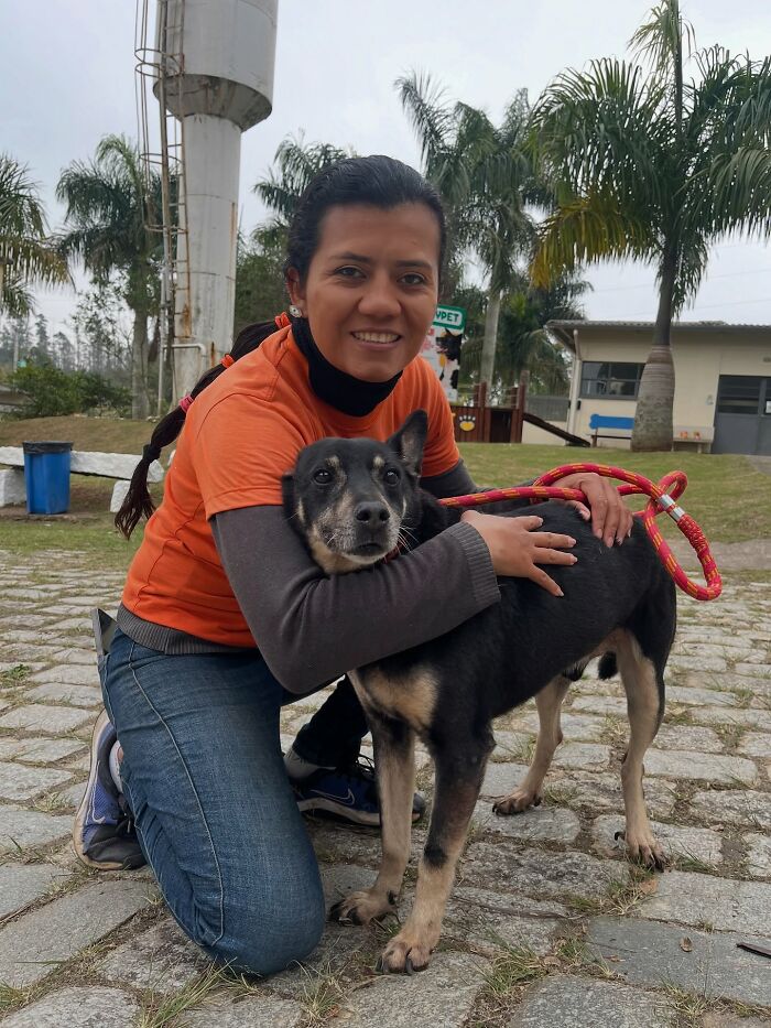Woman smiling and hugging a shelter dog on their weekly walk in an outdoor park setting with palm trees.