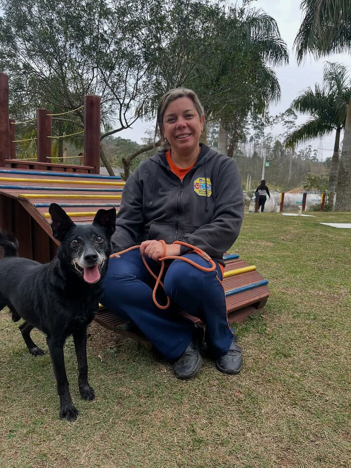 Woman sitting beside a happy black shelter dog on a colorful playground during their weekly walk outdoors.