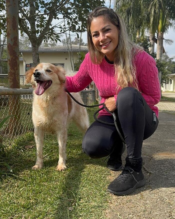 Woman in a pink sweater smiling while holding the leash of a happy shelter dog during a joyful weekly walk outdoors