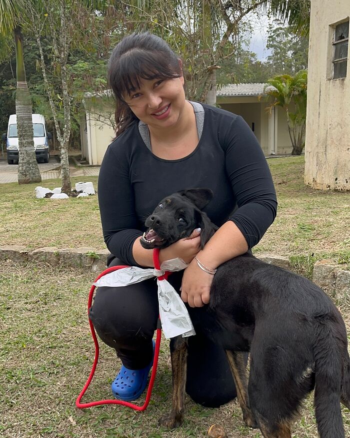 Woman smiling and hugging a joyful shelter dog on a grassy area during one of their weekly walks.