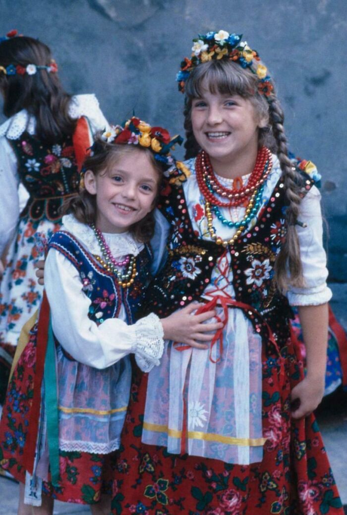 Two smiling girls wearing traditional floral folk costumes and colorful beaded necklaces in a candid glimpse into the past
