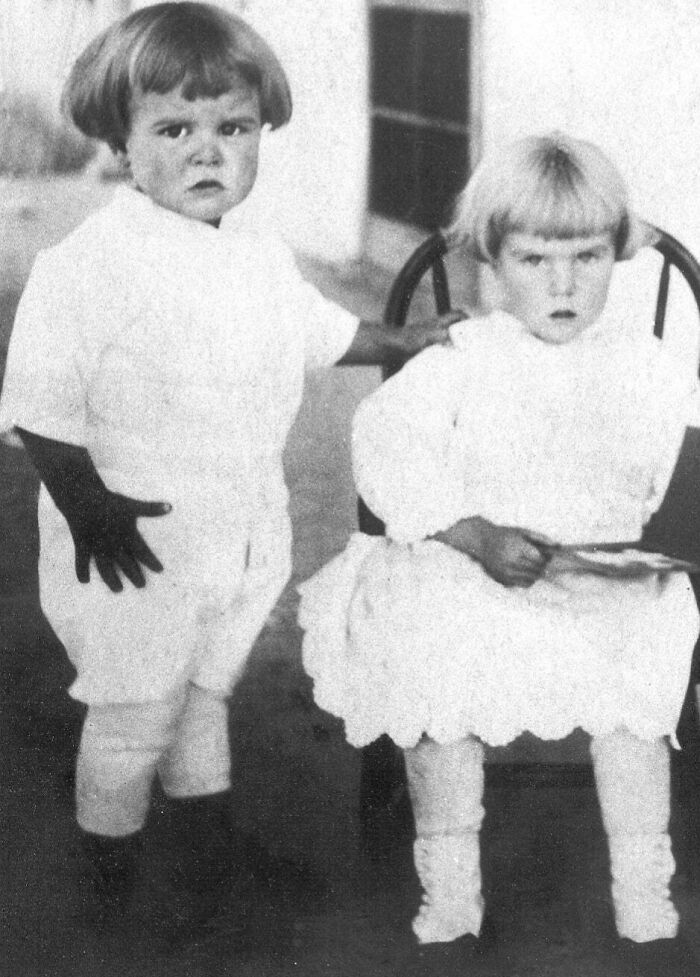 Two young children in vintage clothing, captured in a candid glimpse into the past from historical photographs.