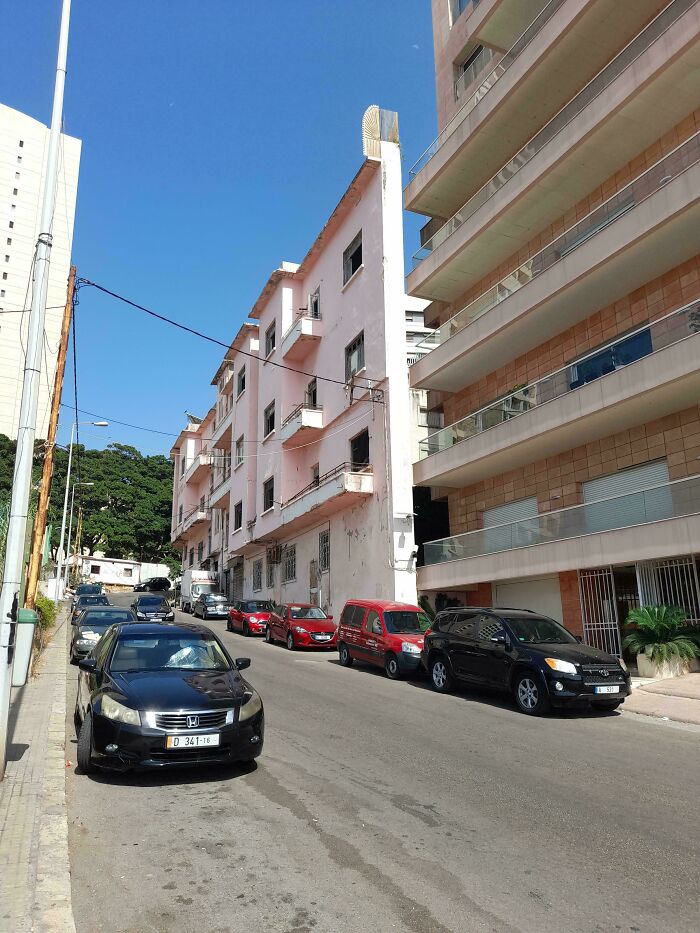 Street view of parked cars and aging buildings in urban hell scene highlighting city decay and societal issues.