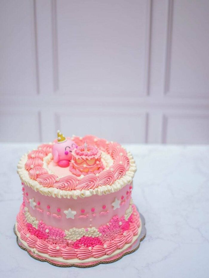 Pink decorated birthday cake with intricate piping and a small figure, showcasing gorgeous baked goods artistry.