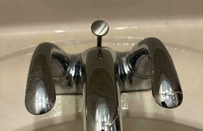 Close-up of a scratched bathroom faucet with a reflective surface, showing a moderately interesting everyday object.