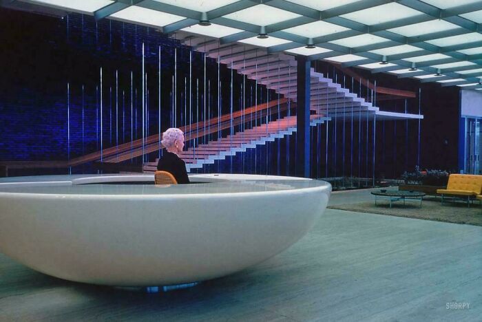 Woman seated in a large modern designer bowl chair inside a stylish minimalist interior with a floating staircase.