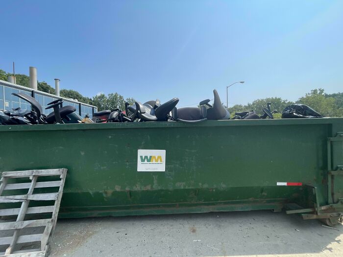 Large green dumpster filled with discarded chair parts representing harsh realities of consumerism waste.