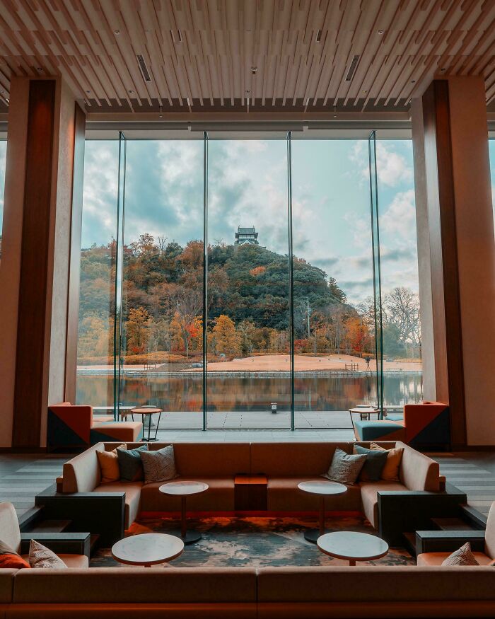 Modern living room with large glass windows showcasing impressive architectural feats and scenic autumn landscape outside.