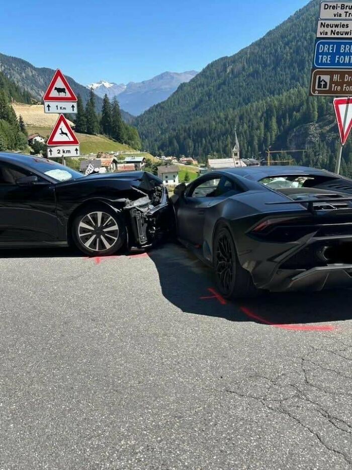 Two black luxury cars involved in a head-on collision on a mountain road. This accident looks expensive.