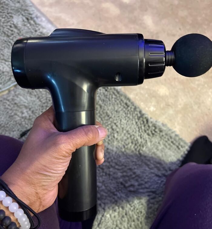 Hand holding a black massage gun with round head attachment, one of the most add to cart worthy finds trending on Amazon.