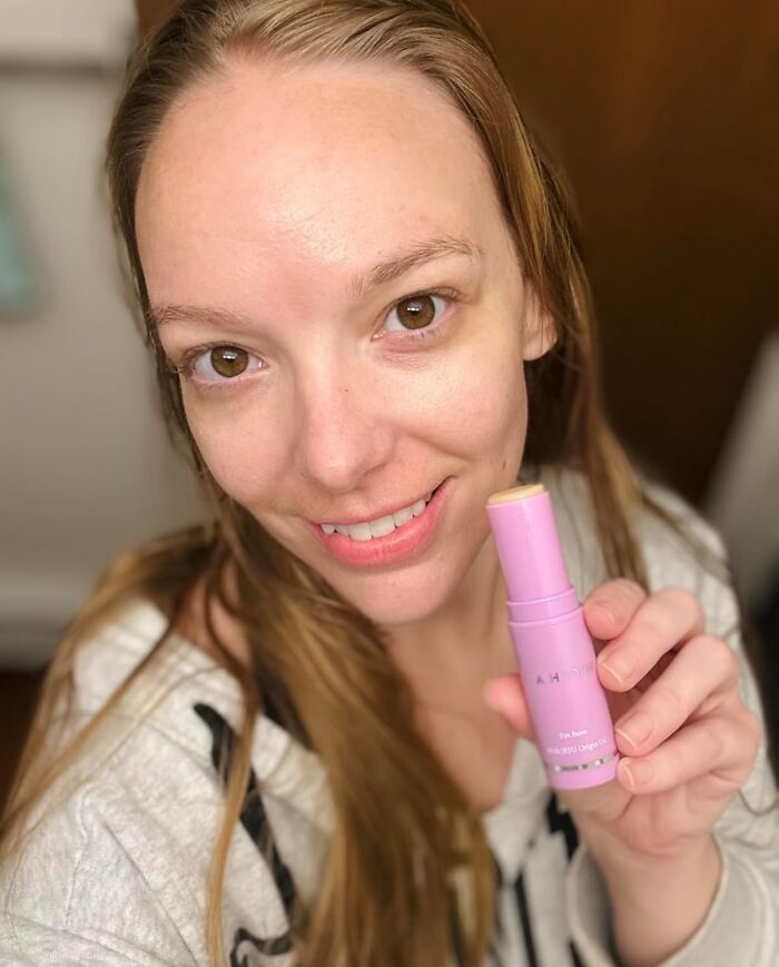 Smiling woman holding a pink beauty product stick, showcasing one of the most add to cart worthy finds trending on Amazon.