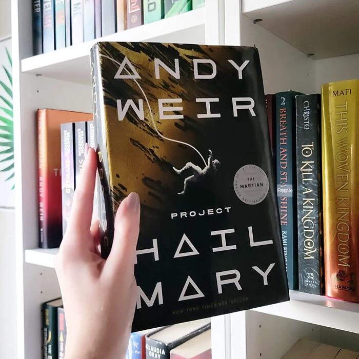 Hand holding Project Hail Mary book among other books, showcasing add to cart worthy finds trending on Amazon.