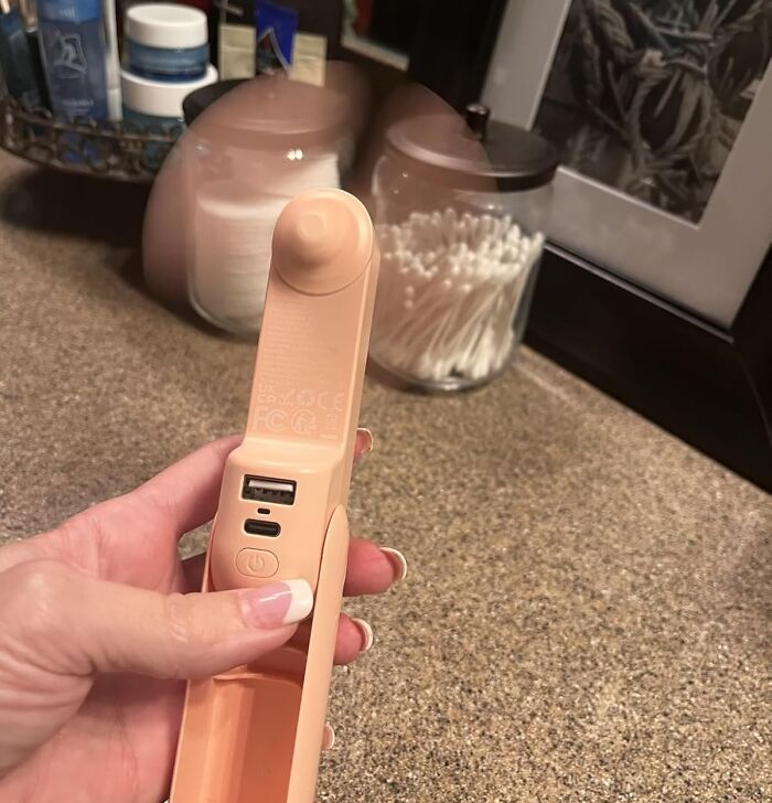 Hand holding a trending Amazon gadget with USB ports on a bathroom countertop near skincare products and cotton swabs.