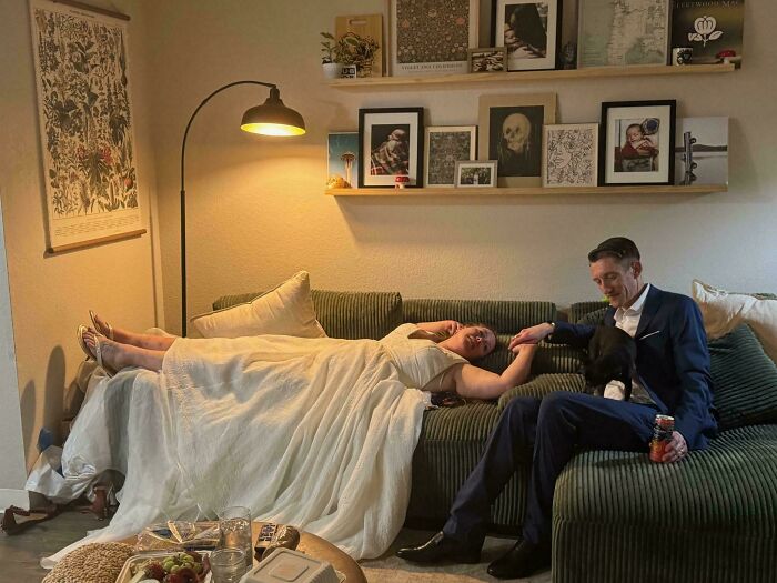 A couple in elegant attire on a couch with vintage framed art, creating an accidental Renaissance photo moment.