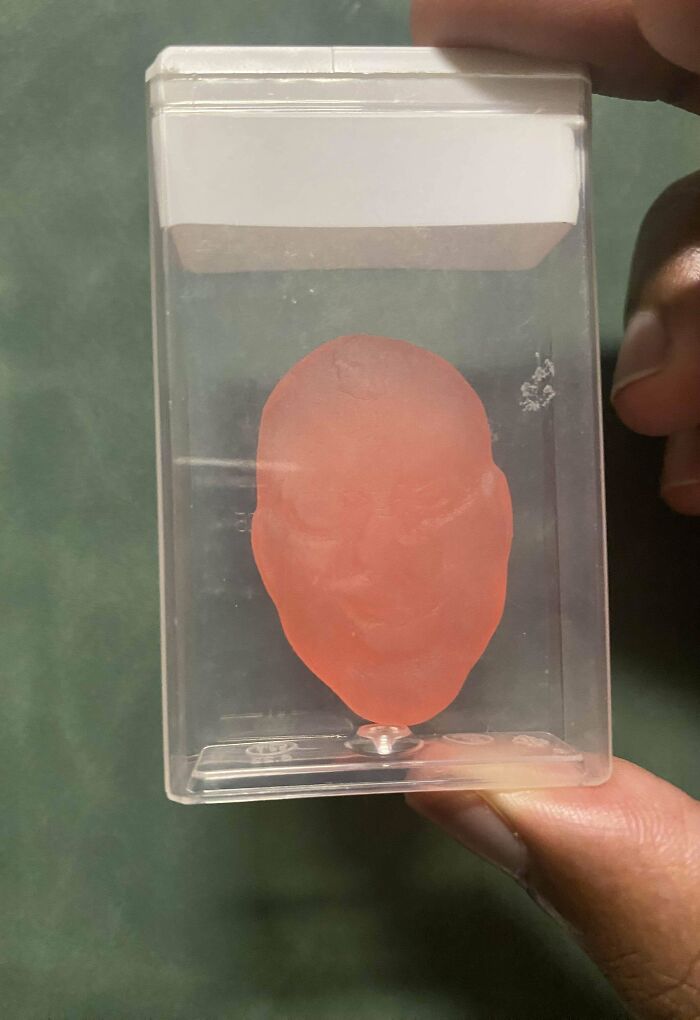 A hand holding a plastic container with a pink wax face mold inside, showcasing a perfectly preventable fail.