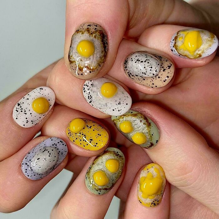 Nails painted with 3D fried egg designs, showcasing funny examples of awful taste but great e*******n in nail art.